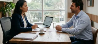 Profissional em mesa de escritório conversando com cliente de forma consultiva sobre termos contratuais e serviços.