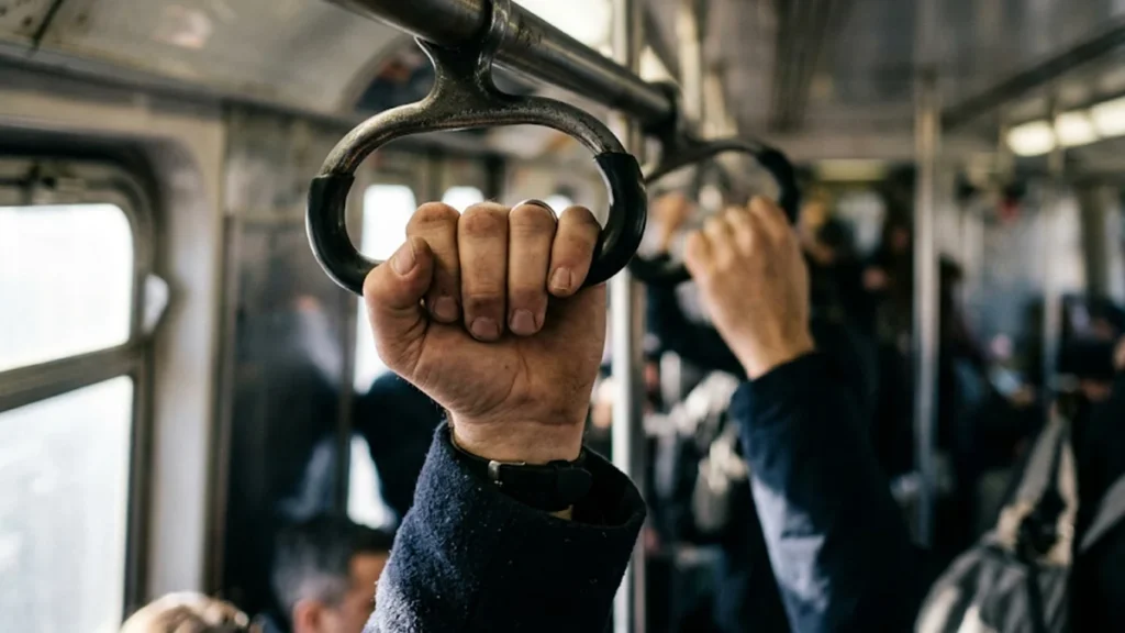 Trabalhador segurando o apoio de um transporte coletivo durante o deslocamento diário para o trabalho.