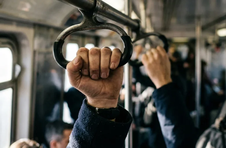 Trabalhador segurando o apoio de um transporte coletivo durante o deslocamento diário para o trabalho.