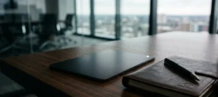 Mesa de reunião moderna em madeira escura com tablet e caneta, ilustrando o ambiente corporativo de resolução de conflitos contratuais por atraso de repasse de aluguel por plataformas digitais.
