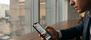 Close de pessoa em escritório moderno em São Paulo segurando celular com perfil do Instagram desfocado, expressando angústia após demissão por justa causa.