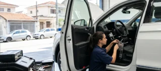 Técnica automotiva em São Paulo inspeciona mecanismo de adaptação manual em um veículo zero quilômetro com a porta aberta, em uma oficina especializada.